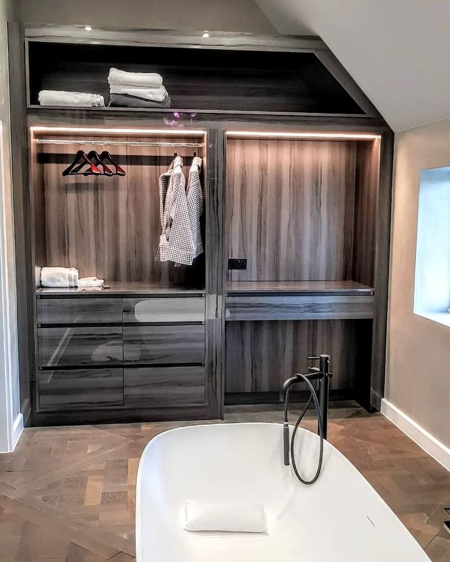 Walk-in wardrobe in walnut beside a freestanding bath